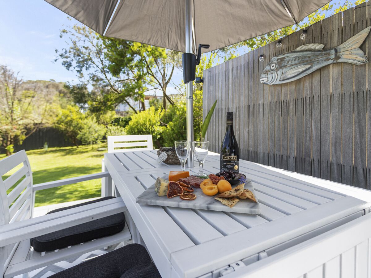 A white outdoor table with a wine bottle, glasses, and a variety of cheeses and crackers.