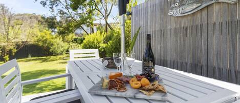 A white outdoor table with a wine bottle, glasses, and a variety of cheeses and crackers.