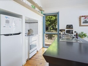 Eine moderne Küche mit weißen Schränken, einem eingebauten Backofen, einer Mikrowelle und einem Toaster. Ein Fenster bietet Blick auf Grünfläche.