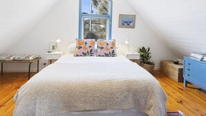 Ein Schlafzimmer mit einem großen Bett, einem Fenster mit Blick, einem Nachttisch mit Lampe und einem kleinen Tisch mit Korb.