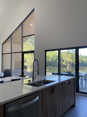 A modern kitchen with a large island, a built-in dishwasher, and a view of a lake through large windows.