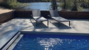 Ett område vid poolen med solstolar och utsikt över en sjö som omges av träd.