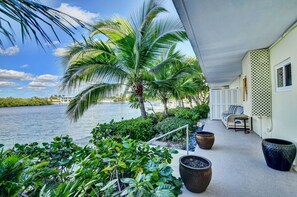 A covered outdoor area with a view of a body of water, palm trees, and potted plants.