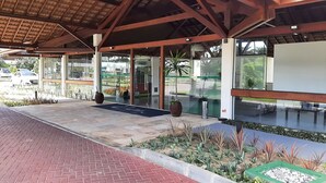 Área externa coberta com piso pavimentado, portas de vidro e plantas em vasos.