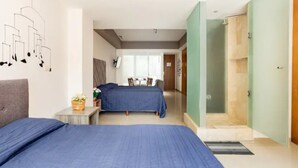 Camera d'albergo moderna con due letti, un tavolino con una pianta e zona doccia.