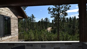 Una cabaña de madera con chimenea de piedra, un sillón negro y vista al bosque.