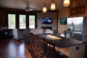 A modern kitchen with a central island, wooden bar stools, a built-in refrigerator, and a stone fireplace. - Sunset Ridge Cabin (lead)