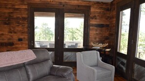 Una habitación con paredes de madera, un sofá gris, un sillón gris y vistas a través de amplias ventanas.