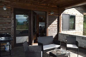 A covered outdoor area with wicker furniture, a grill, and a stone fireplace. - Sunset Ridge Cabin (lead)