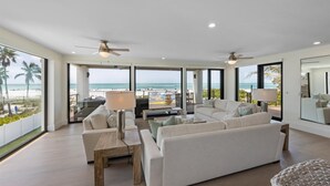 A spacious living room with a large window overlooking the beach, a ceiling fan, and a comfortable seating area. - True Beachfront!  2 Beachfront Masters - Best Location!! (Anna Maria Island)