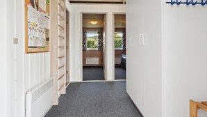 Un pasillo con una escalera de madera, un tablón de anuncios y un perchero azul.