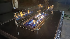 Uma lareira ao ar livre com mesa de vidro e vários queimadores.
