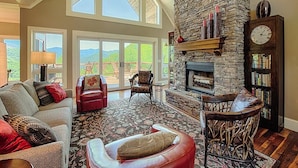A spacious living room with a stone fireplace, a large window, and a cozy seating area.