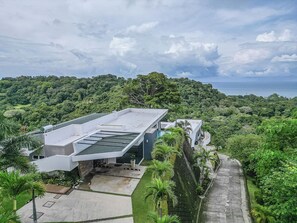 Un edificio moderno con techo plano, rodeado de abundante vegetación y un cielo despejado.