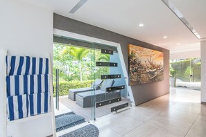 A modern interior with a glass staircase, a seating area with cushions, and a large painting of boats.