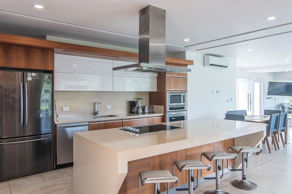 A modern kitchen with stainless steel appliances, a central island with bar stools, and a large TV mounted on the wall.