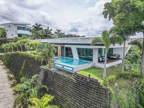 A modern house with a swimming pool, surrounded by lush greenery and a brick wall.