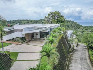 A modern house with a flat roof, surrounded by lush greenery and a clear view of the ocean.