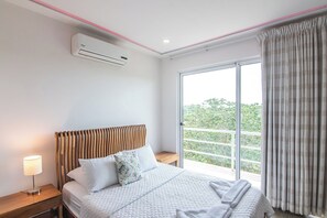 Et hotelværelse med seng, et natbord, en aircondition og et vindue med gardiner, samt udsigt til grønne områder.