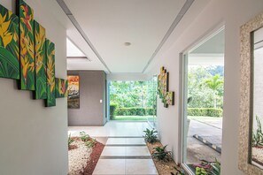 A modern hallway with a glass door leading to a garden, a painting on the wall, and a tiled floor.