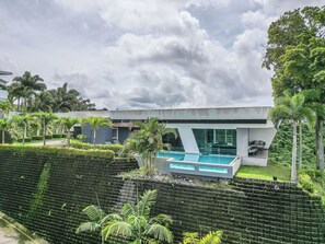 Et moderne hus med swimmingpool, omgivet af frodig vegetation og en overskyet himmel.