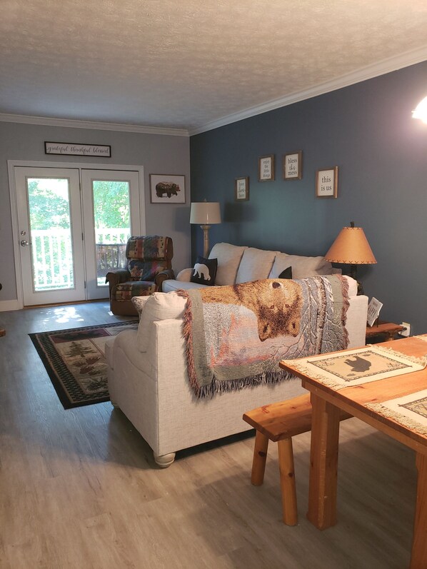 A cozy living room with a white couch, a wooden coffee table, and a rug. There is a door with glass panels leading to a balcony.