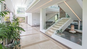 A spacious, modern interior with a high ceiling, a staircase with glass railings, and a view of the outdoors. - Luxury 4BR Ocean View with Infinity Pool & Jacuzzi (Playa Hermosa)