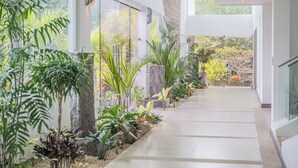 A modern indoor corridor with glass doors leading to a garden area, surrounded by various plants and a tiled floor. - Luxury 4BR Ocean View with Infinity Pool & Jacuzzi (Playa Hermosa)