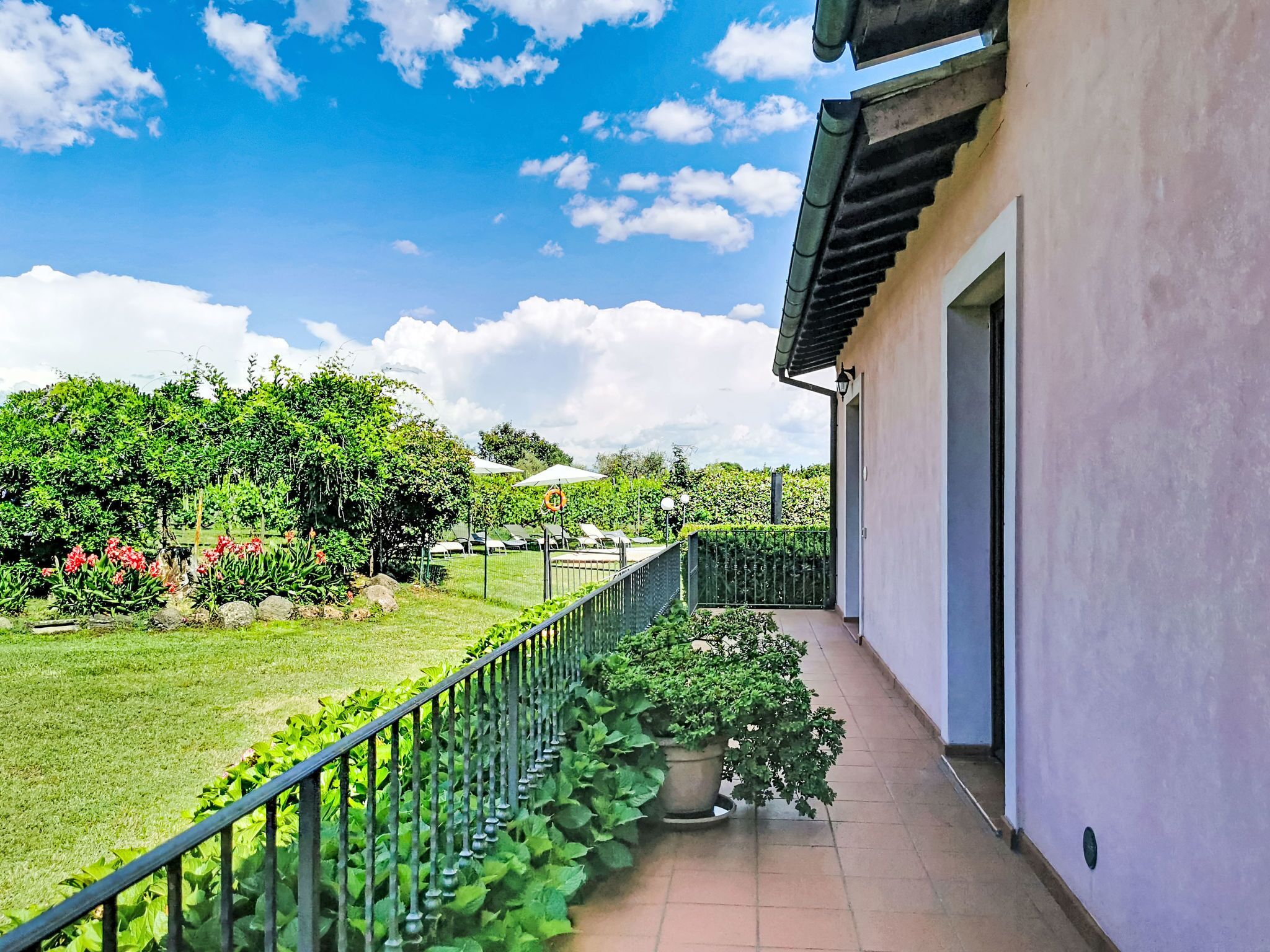 A balcony with a view of a garden, a fence, and a building with a door.