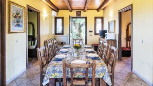 A dining area with a long table, chairs, a vase with flowers, and a television on a cabinet. - La Quercia by Interhome (Orte)