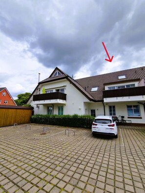 A residential building with a tiled roof, a balcony, and a parked car in the driveway.