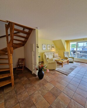 A living room with a wooden staircase, a sofa, a coffee table, and a vase of flowers.