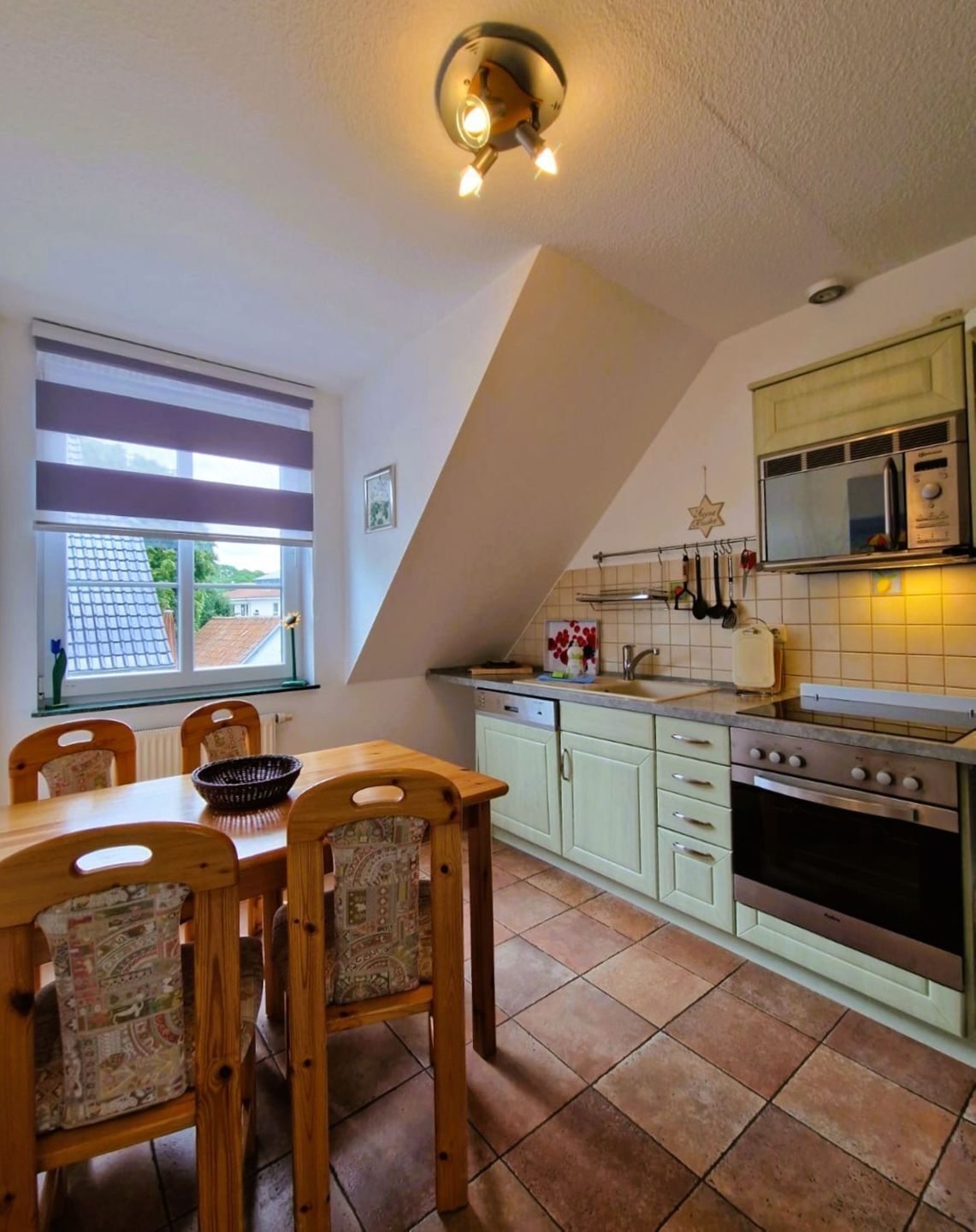 Una cocina con una mesa de comedor, sillas, estufa y ventana con persianas.