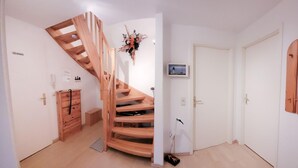 Eine Holztreppe führt zu einer zweiten Etage, eine weiße Tür mit einem Bild und eine Wand mit Holzvertäfelung.