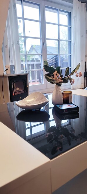 A room with a glass-top table, a white ceramic bowl, a vase with flowers, a box of tissues, and a small heater.