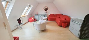 A room with a white sofa, a red couch, a small white table, a red bean bag chair, a grey dresser, and a TV on a stand.