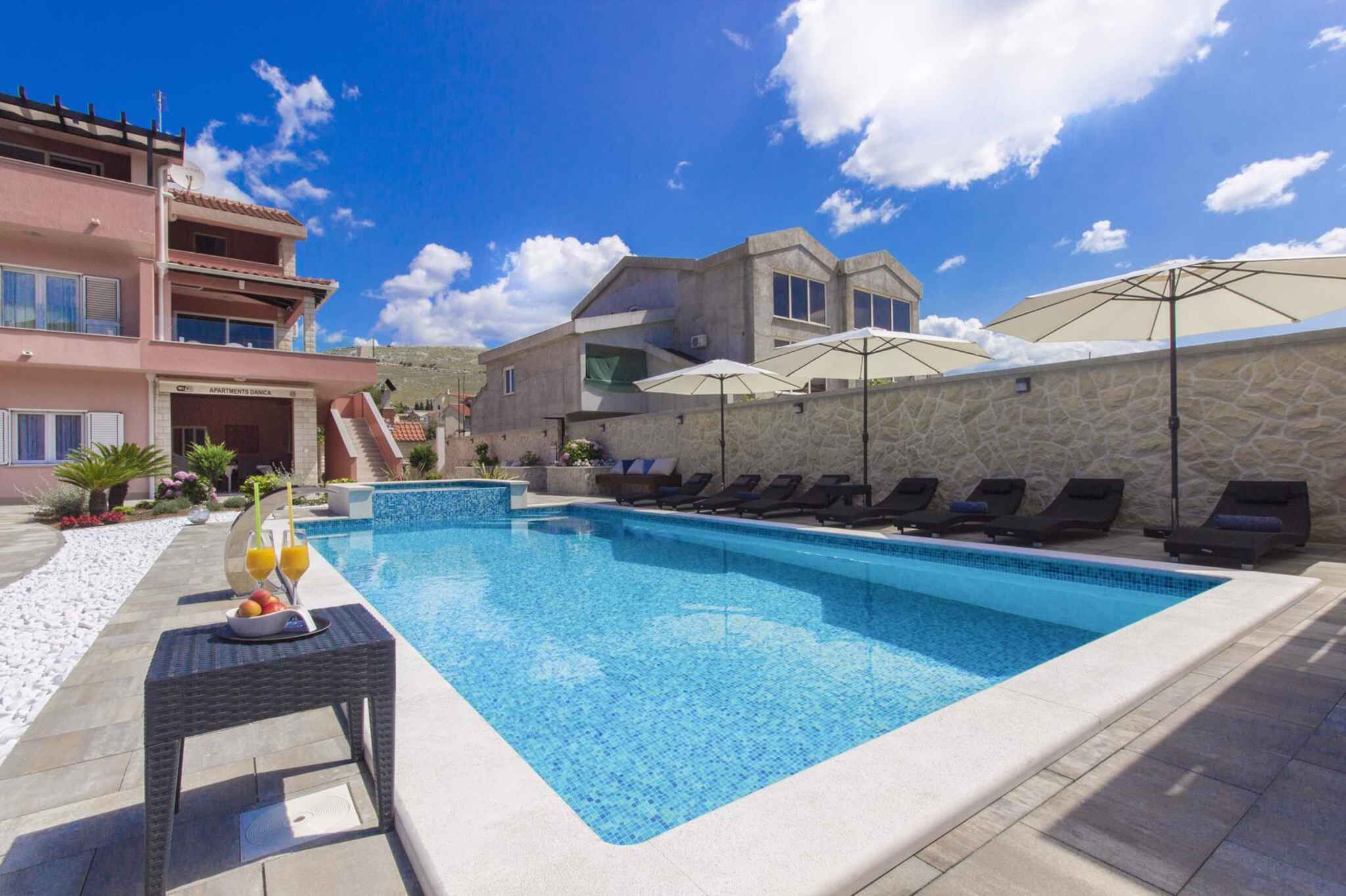 Une piscine avec des chaises longues et des parasols, un mur en pierre et un bâtiment doté de balcons.