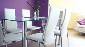 A dining area with a glass table surrounded by white chairs, a vase with flowers, and a purple wall.