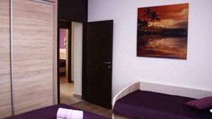 A hotel room with two beds, a wooden wardrobe, and a painting of a sunset over the ocean.