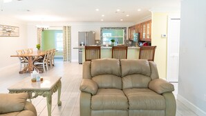 A spacious living room with a beige sofa, a dining area with wooden chairs, and a kitchen with wooden cabinets. - Blue Haven Retreat Spacious 3BR, 2BA Escape (Sebastian)