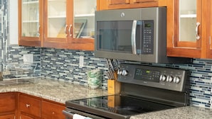 A kitchen with wooden cabinets, a stainless steel oven, a microwave, and a granite countertop. - Blue Haven Retreat Spacious 3BR, 2BA Escape (Sebastian)