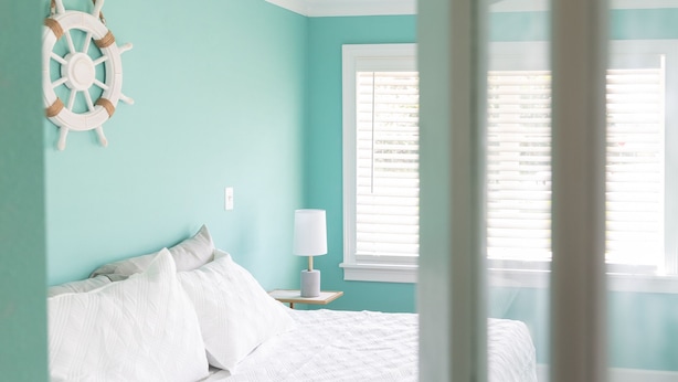 A bedroom with a bed, a nightstand, a wall-mounted ship's wheel decoration, and a window with blinds. - Blue Haven Retreat Spacious 3BR, 2BA Escape (Sebastian)