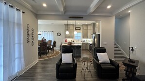 A modern living room with two black leather sofas, a dining area with a round table, and a kitchen with grey cabinets and stainless steel appliances. - Modern New 3bd/3.5ba Close To Everything! (Jeffersonville)