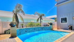 A clear blue pool surrounded by palm trees and a white building with pool rules posted. - In-town coastal getaway, with a heated pool & level 2 Tesla EV charger on site. (Port Aransas)