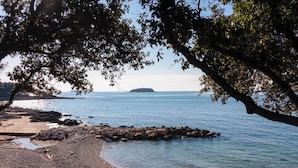 Une plage bordée d’un rivage rocheux, aux eaux calmes, avec une île visible au loin.