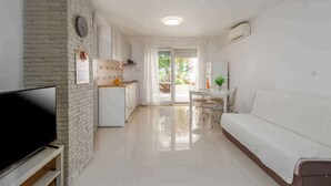Un salon moderne doté d’un téléviseur à écran plat, d’un canapé blanc et d’un coin repas avec une table et des chaises.