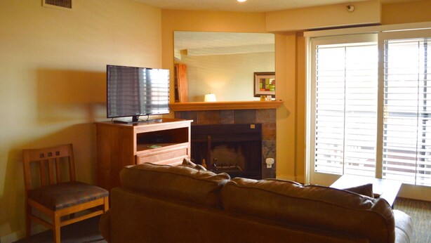 A living room with a television on a wooden stand, a fireplace, a sofa, and a chair.