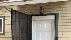 A white door with a black mesh screen, a green door frame, and a small outdoor light fixture above it. - Newly redone studio w/outdoor lawn & eating space (Azusa)