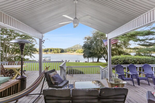 A covered deck with outdoor furniture, a view of a lake, and an American flag.