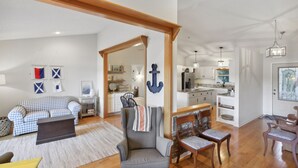 A spacious living area with a checkered sofa, a grey armchair, and a wooden dining table. A kitchen with white cabinets and a hanging light fixture is visible in the background. - Lake front home (Hiawassee)